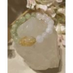 Handmade prehnite, rose quartz, and citrine gemstone bracelet with soft green and white beads displayed on a crystal stone background.