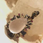 Handmade silver pendant featuring a drop-shaped rose quartz gemstone surrounded by ruby and sapphire accents in an intricate floral-inspired design with gold and dark silver details.