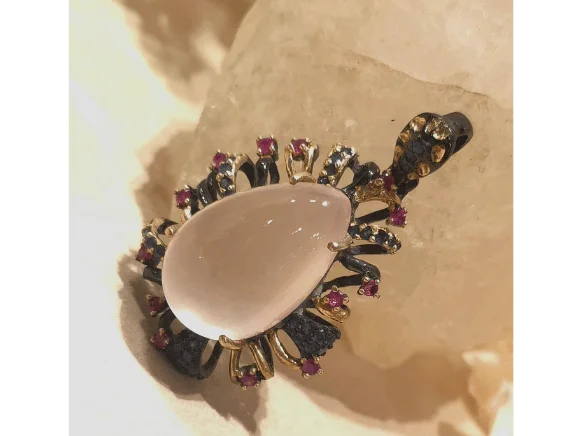 Handmade silver pendant featuring a drop-shaped rose quartz gemstone surrounded by ruby and sapphire accents in an intricate floral-inspired design with gold and dark silver details.