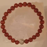Handcrafted Carnelian gemstone bracelet with polished 6mm red-orange beads and a sparkling gold-toned centerpiece, symbolizing protection from the evil eye, courage, and positive energy.