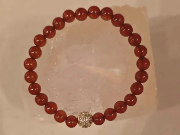 Handcrafted Carnelian gemstone bracelet with polished 6mm red-orange beads and a sparkling gold-toned centerpiece, symbolizing protection from the evil eye, courage, and positive energy.