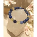 Handmade sodalite, prehnite, and amethyst gemstone bracelet with 10 mm beads displayed on a natural crystal stone, featuring deep blue, golden-green, and violet tones.