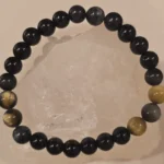 Handmade 8mm Obsidian and Hawk’s Eye gemstone bracelet displayed on a clear quartz crystal, symbolizing protection, intuition, focus, and evil eye defense.