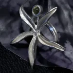 Handcrafted sterling silver flower ring featuring a natural 6mm green Peridot (Olivine) gemstone displayed on a decorative dark background.