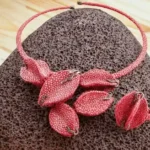 Handcrafted red stingray leather choker necklace with matching ring displayed on a volcanic stone.