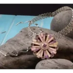 Handcrafted sterling silver enamel pendant with two artistic silver necklaces displayed on natural stones.